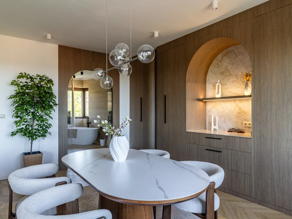 Dining area with an arched, illuminated shelf niche and a wooden furniture wall